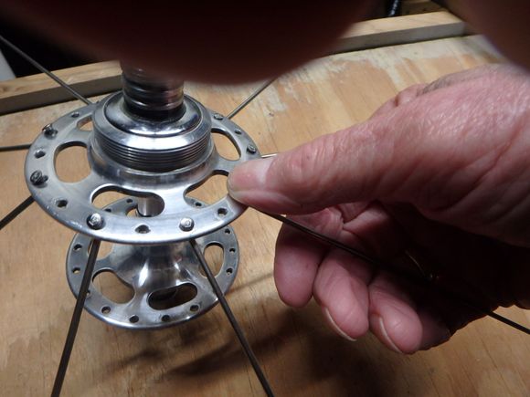 The spokes are being bent upward from the hub to seat the spoke end, and make the lacing easier when we get to the final step.