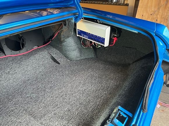 The carpeted trunk floor and the 8-channel amp.  The amp is mounted to a 1/2" piece of plywood that I screwed to the metal "fin" that hangs down where the 