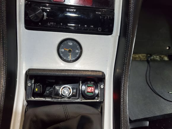 Push button switch mounted in ashtray next to dual USB charging ports with voltage gauge and remote USB stick for stereo MP3s