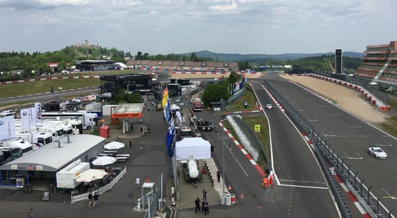 View from the Rowe lounge. Too the right it is the exit from Nordschleife. To the left the entrance from the GP track to Nordschleife.
The Nürburg Castle to the left then you see the T13 Tribune where the old pit lane is which is used by the Industrial pool and races where the GP-track is not used. For instance some of the RCN-races. I think this is the highest part of the Nordschleife. in the background you can see what once where an volcano. It is Hohe Acht.