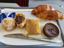 The sweet meal replacement. I was semi-curious to see if it would actually replace the entire meal or just the main course. It actually replaces everything! You only get to pick a bread roll or croissant, nothing else from the regular "sides". It even comes in a smaller tray, like the ones used on domestic flights (?).
2 pieces of that thing on the left, hard, bitter chocolate inside, not bad, one piece of don't-know-what-it-was in the middle, like halva but with a taste like galaktompoureko :D
