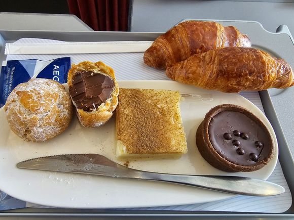 The sweet meal replacement. I was semi-curious to see if it would actually replace the entire meal or just the main course. It actually replaces everything! You only get to pick a bread roll or croissant, nothing else from the regular "sides". It even comes in a smaller tray, like the ones used on domestic flights (?).
2 pieces of that thing on the left, hard, bitter chocolate inside, not bad, one piece of don't-know-what-it-was in the middle, like halva but with a taste like galaktompoureko :D
