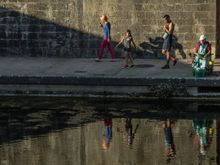 Little girl turns to watch seated fisherman.