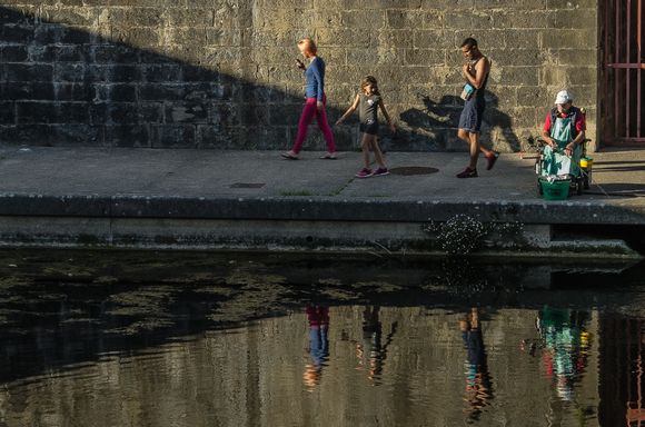 Little girl turns to watch seated fisherman.