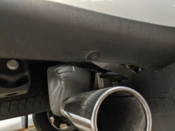 Bolt above tailpipe - replaces plastic push - clip. Driver side similar