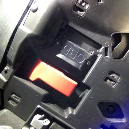 The OBDII port it protected by a flap, open flap located near the hood release under the steering column.