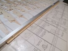 It took awhile, but I finally freed all of the wing ribs from their sheets.  It's time to dry fit the ribs to the bottom spar.  Notice that I've butted the spar to a known straight aluminum square stock.  I never trust the straightness of lines on plans...