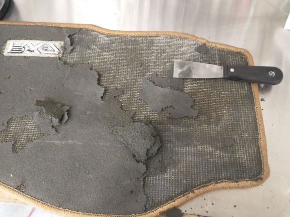 Here's a shot of the passenger side mat underside as it was. I used a putty knife to scrape off all the old foam. In some parts where the foam was still flexible and not crumbling, you can use the knife to start on an edge, and pull the rest off slowly with your fingers. This leaves a little bit of foam behind, but I just used a Scotch Brite pad to scrub off whatever was left.